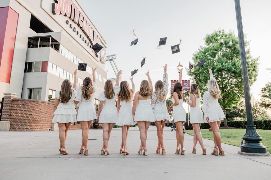 senior photos photographer near me | Senior girls dressed in white dresses toss cap and gown