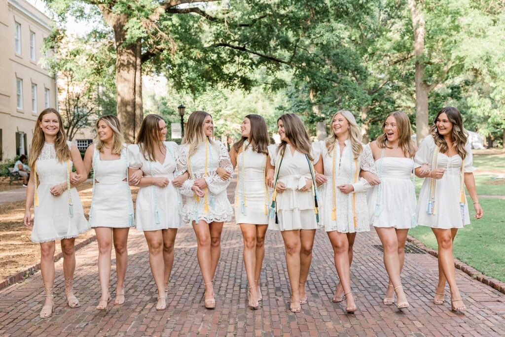 senior photos photographer near me | Group of senior girls dressed in white dresses walking during senior session