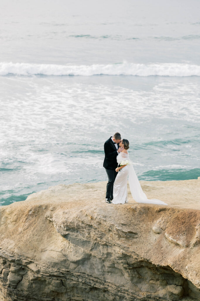 luxury wedding ideas | Couple kissing on cliff in front of pacific ocean