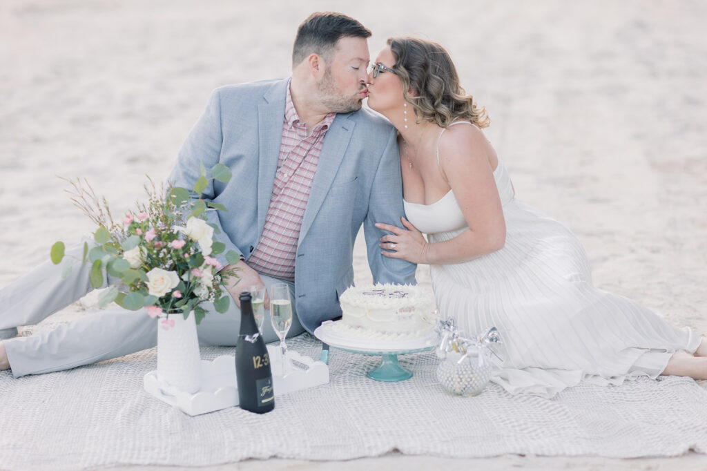 Engagement photographer near me | couple kissing on the beach with a blanket and cake