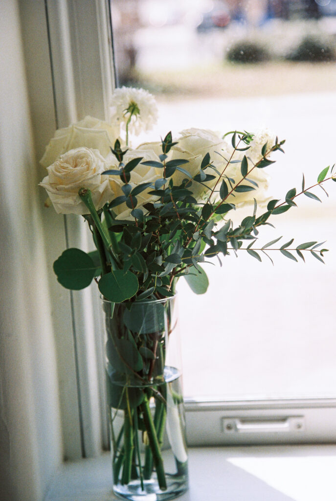 Film Photographer | Photo of white roses and floral pieces in vase on window. 35mm color film photographed before wedding. Wedding photos at 701 Whaley in Columbia, South Carolina.