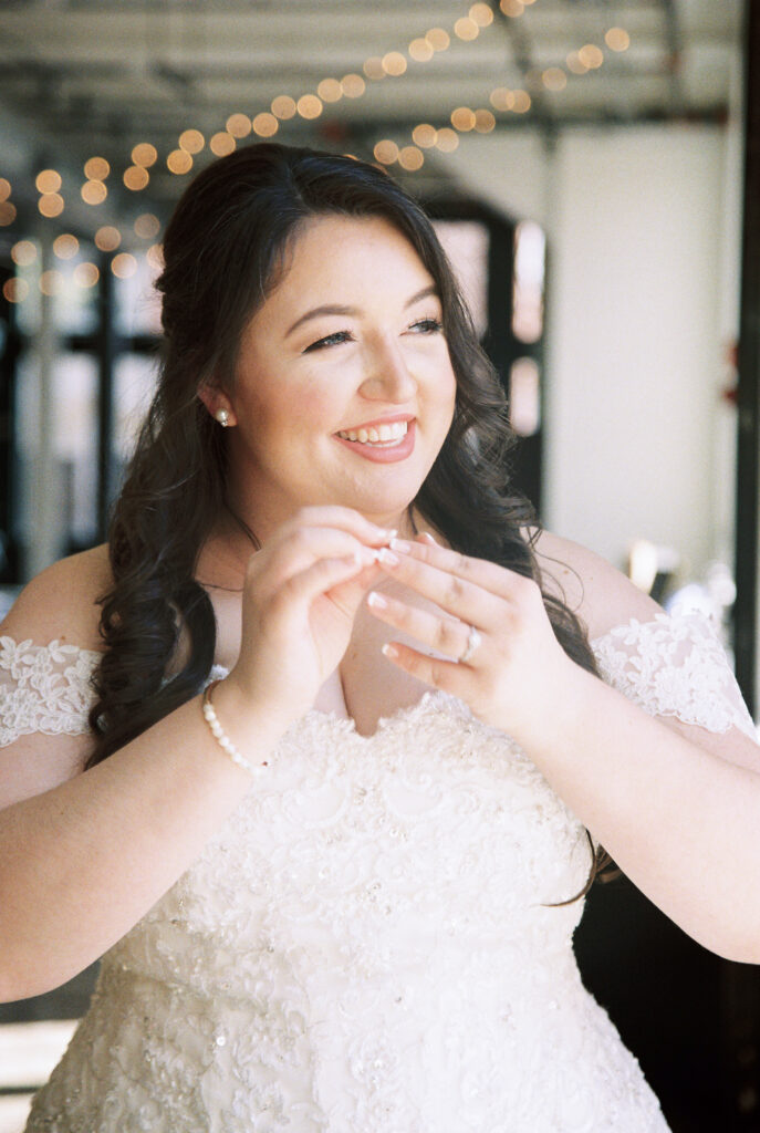 Film Photographer | Bride smiling and looking out the window while putting her earrings in. 35mm color film photographed before wedding. Wedding photos at 701 Whaley in Columbia, South Carolina.