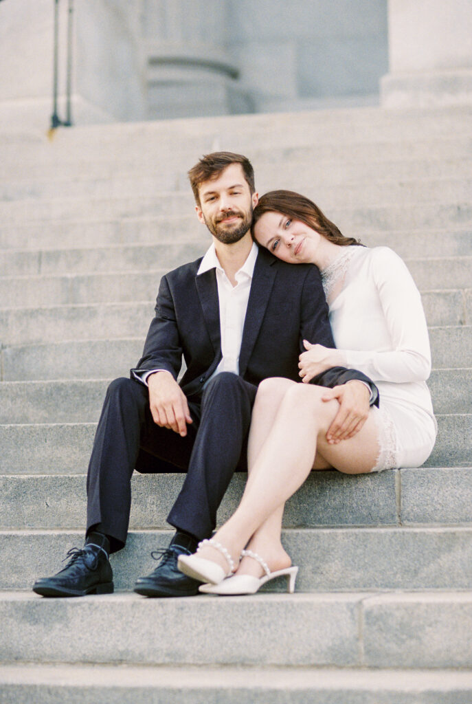 Film Photography | Couple looking at the camera while sitting on the SC Statehouse Steps, during engagement session in Columbia, South Carolina. Photographed in 35mm color film.