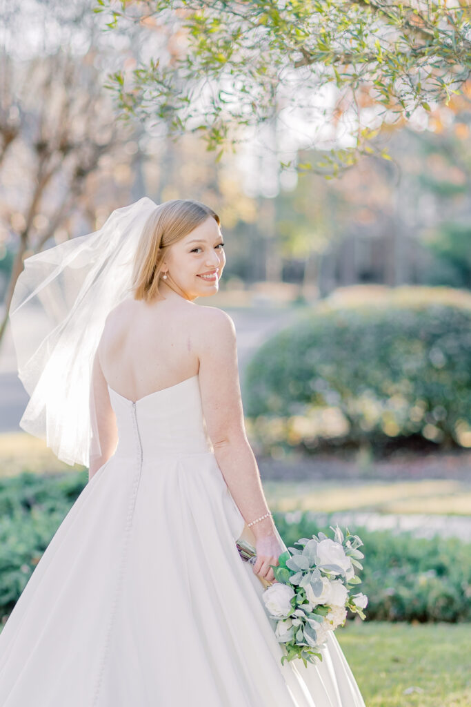 Bridal Portraits | Bride looking at the camera and holding her veil. Warm summer day in Charleston, SC.