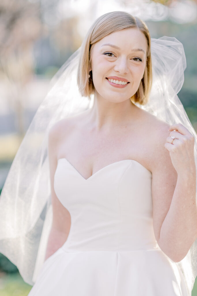 Bridal Portraits | Bride looking at the camera and holding her veil. Warm summer day in Charleston, SC.