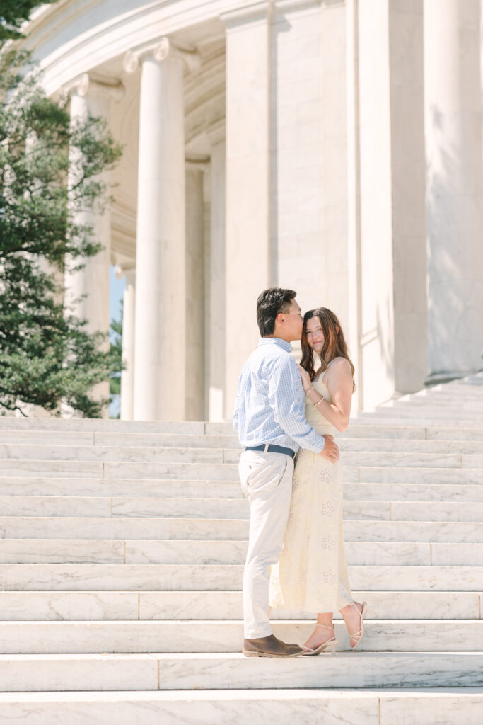 DC Engagement Photographer | Engagement session in Washington, DC | couple holding each other in front of the Thomas Jefferson Memorial while man kisses side of womans head