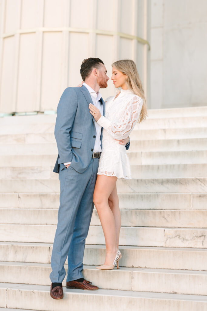 Columbia SC Engagement Photos | Stee Garman Photography Fine-art Wedding Photographer | A couple stands closely on marble steps, gazing into each other's eyes. The man wears a blue suit, the woman a white lace dress. The mood is romantic.