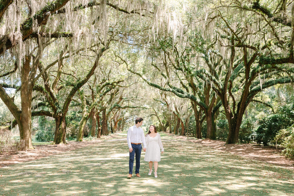 Charleston engagement photographers | Engagement session in Charleston SC | couple walking and holding hands under the canopy of trees covered in spanish moss
