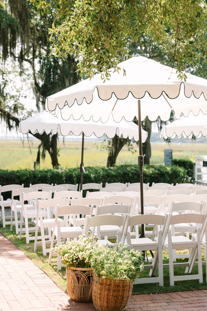 Columbia SC Photography | Stee Garman Photography Fine-art Wedding Photographer | White chairs and parasols set up for an outdoor ceremony under trees, with wicker baskets of flowers, creating a serene and inviting atmosphere.