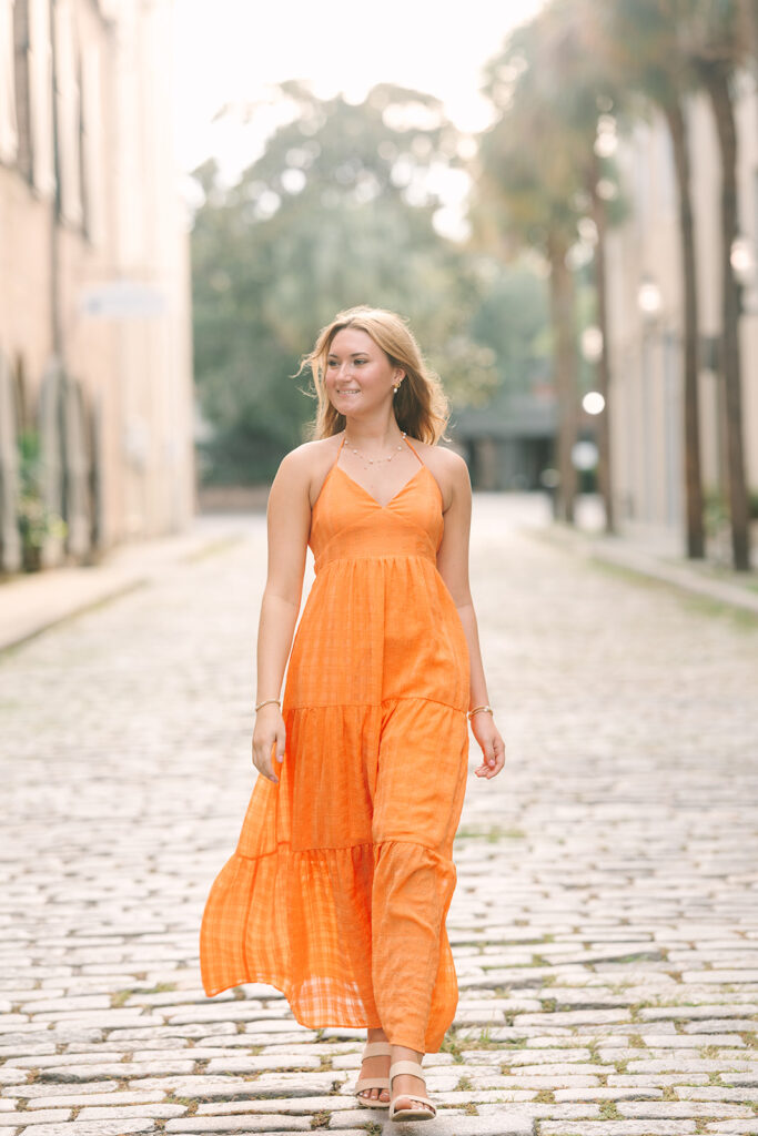 Charleston senior pictures | Senior session in Charleston SC | Senior in orange dress walking down street made of old bricks