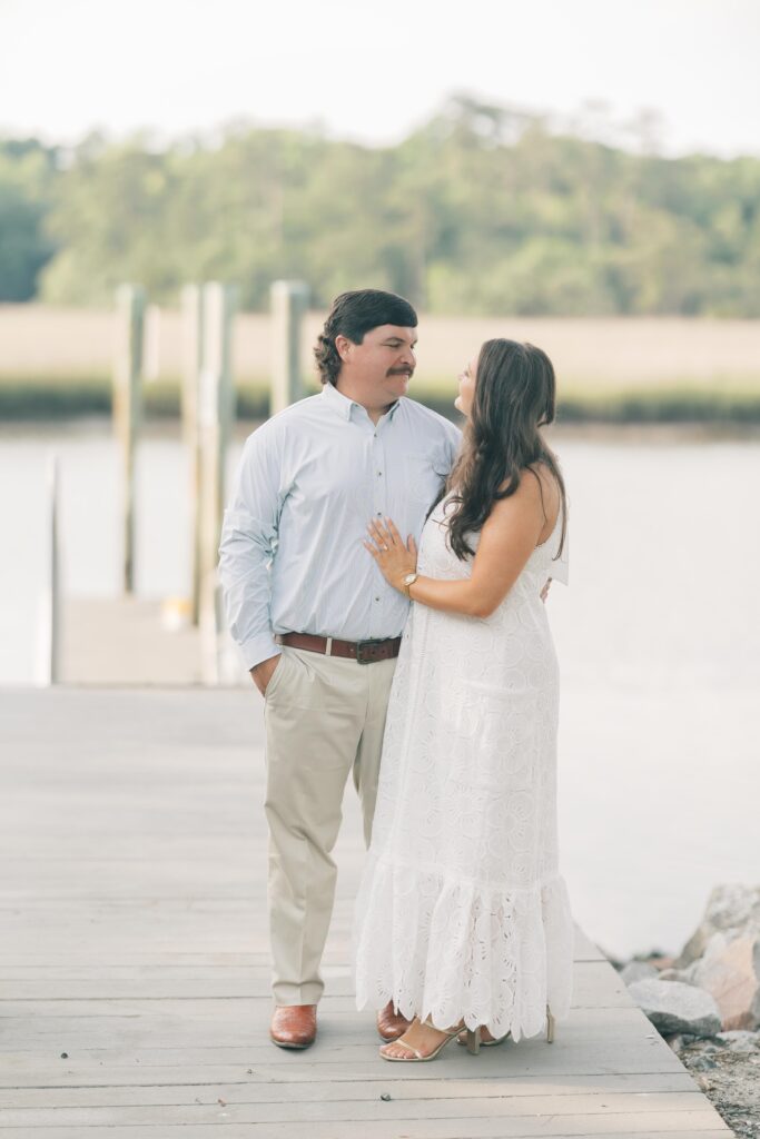 Charleston Wedding Photographer | Engagement Session at Creek at Ion | Couple smiling at each other on dock with creek in the background