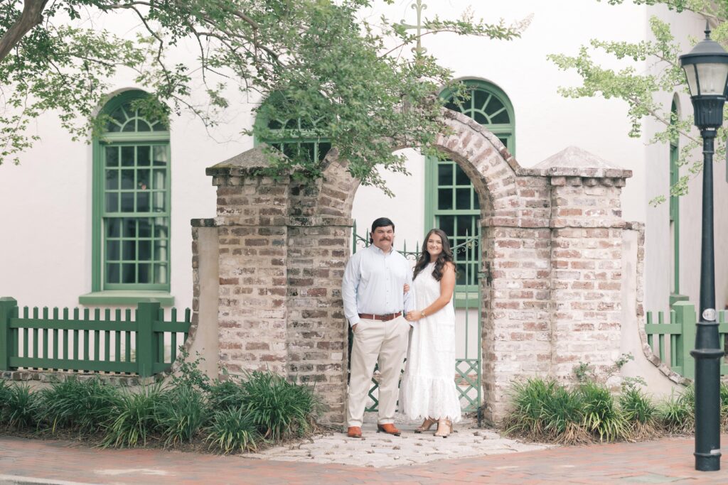 Charleston Wedding Photographer | Engagement Session at Creek at Ion | couple smiling at the camera under brick arch way at creek at ion chapel with green windows