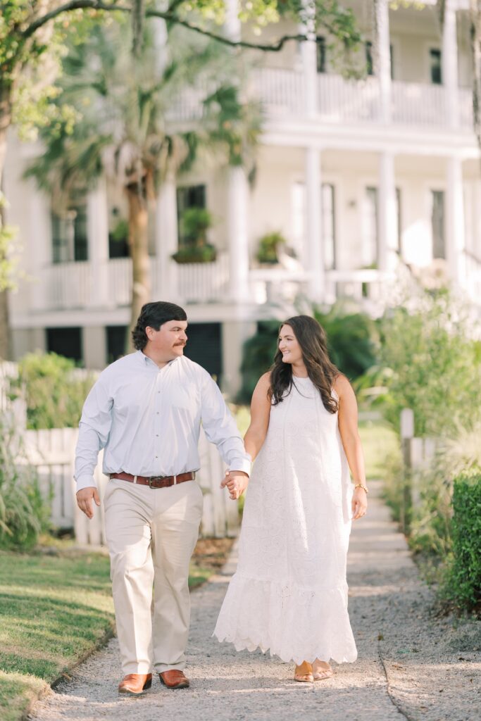 Charleston Wedding Photographer | Engagement Session at Creek at Ion | couple holding hands and smiling with grand white home in the background