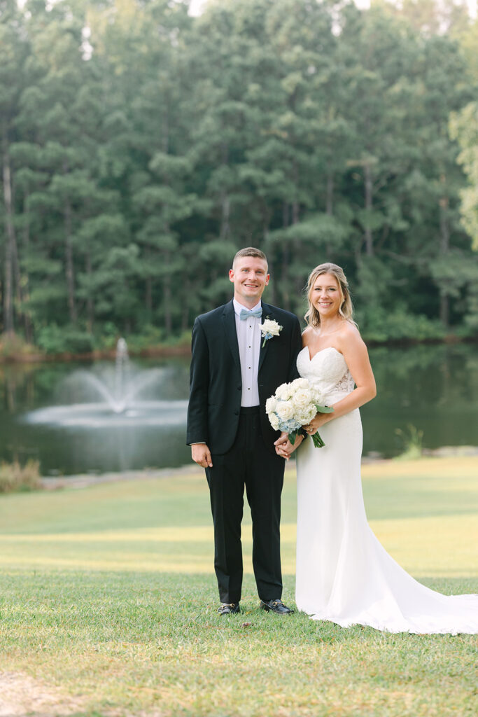 Bride and groom standing together on an open lawn with peaceful pond views and a refined outdoor setting often found at Charleston SC wedding venues on the water.