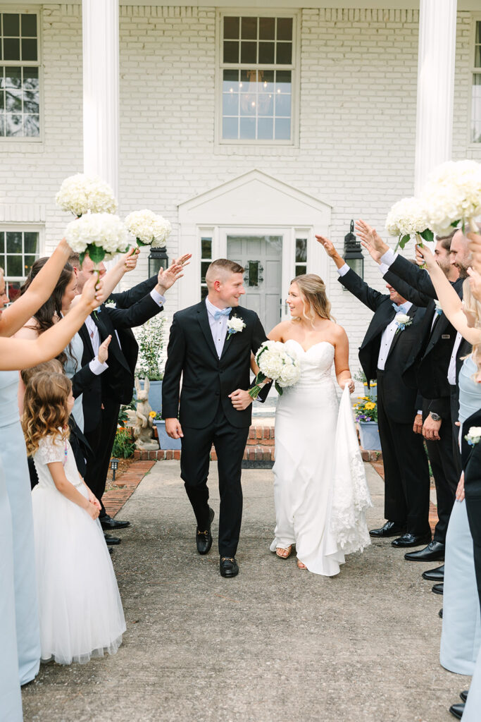 Wedding Photographers in Columbia SC | Stee Garman Photography Fine-art Wedding Photographer | A bride and groom smile at each other while walking down an aisle formed by guests raising white flowers