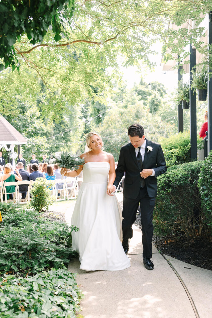 Wedding Photographers in Columbia SC | Stee Garman Photography Fine-art Wedding Photographer | Bride in a white gown and groom in a black suit hold hands, smiling while walking down a garden path.