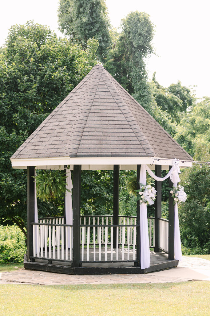 Wedding Photographers in Columbia SC | Stee Garman Photography Fine-art Wedding Photographer | A charming gazebo adorned with white drapery and floral arrangements stands amidst lush greenery