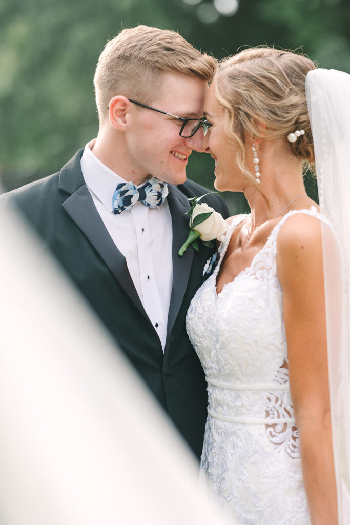 Columbia SC Wedding Photographers | Stee Garman Photography Fine-art Wedding Photographer | A joyful bride and groom, nose-to-nose, share a tender moment. The groom wears a suit with a bow tie, and the bride is in a lace gown with a veil.