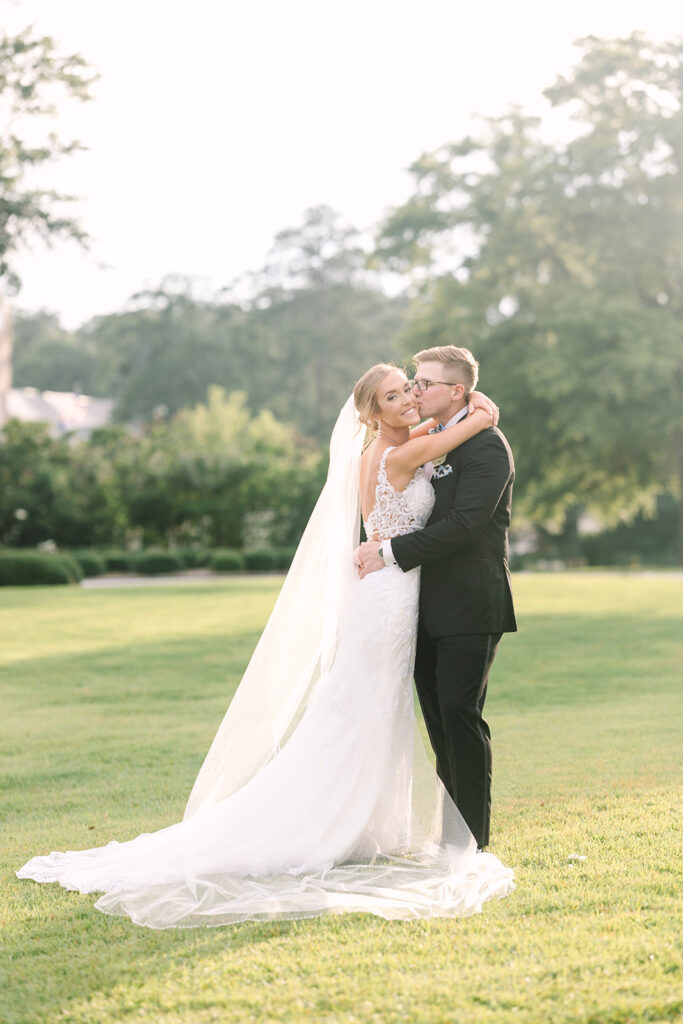 Wedding Photographers in Columbia SC | Stee Garman Photography Fine-art Wedding Photographer | A joyful bride in a white lace gown embraces the groom in a black tuxedo on a sunlit lawn.