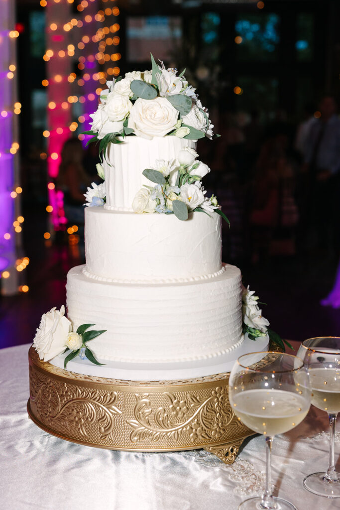 Columbia SC Wedding Photographers | Stee Garman Photography Fine-art Wedding Photographer | Three-tier white wedding cake with white roses and greenery, on an ornate gold stand.