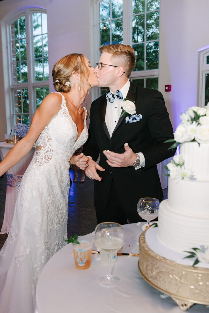 Columbia SC Wedding Photographers | Stee Garman Photography Fine-art Wedding Photographer | Bride and groom lovingly kiss at their wedding, standing by a tiered cake. The bride wears a lace gown; the groom wears a black suit and floral bow tie.