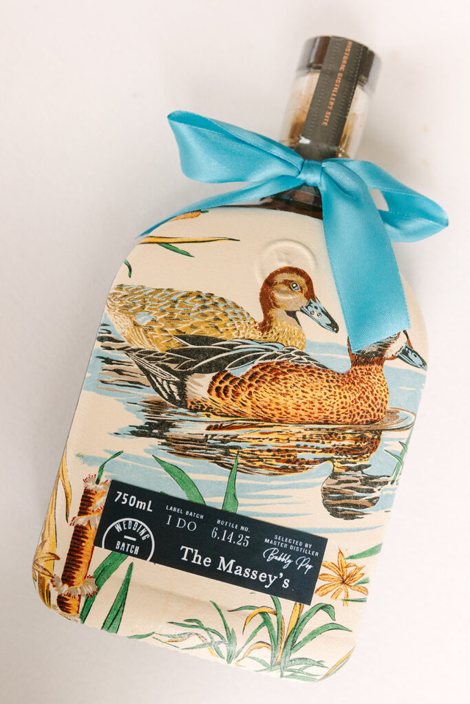 Columbia SC Wedding Photographers | Stee Garman Photography Fine-art Wedding Photographer | A bottle with a botanical design featuring two ducks on a pond. It is adorned with a blue ribbon and labeled "The Massey's"