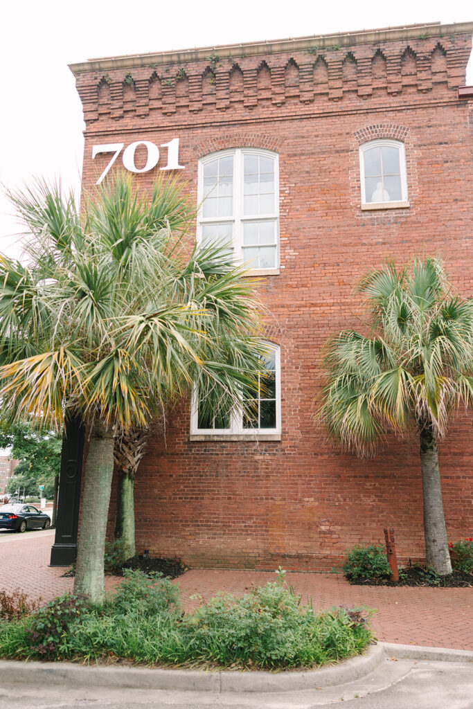 Wedding Photographers in Columbia SC | Stee Garman Photography Fine-art Wedding Photographer | A red brick building labeled "701" with tall arched windows is flanked by two palm trees. 
