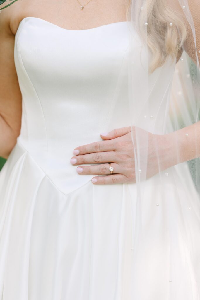 Bridal Portraits Photographer Columbia SC | Stee Garman Photography Fine-art Wedding Photographer | Bride in a strapless white dress gently resting a hand on her waist, showcasing an elegant ring. Her veil, adorned with pearls, adds a soft, romantic touch.