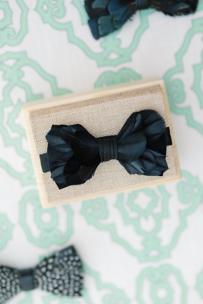 Columbia SC Wedding Photographers | Stee Garman Photography Fine-art Wedding Photographer | Elegant black feathered bow tie on a textured beige box against a decorative light green and white patterned background. Sophisticated and stylish.