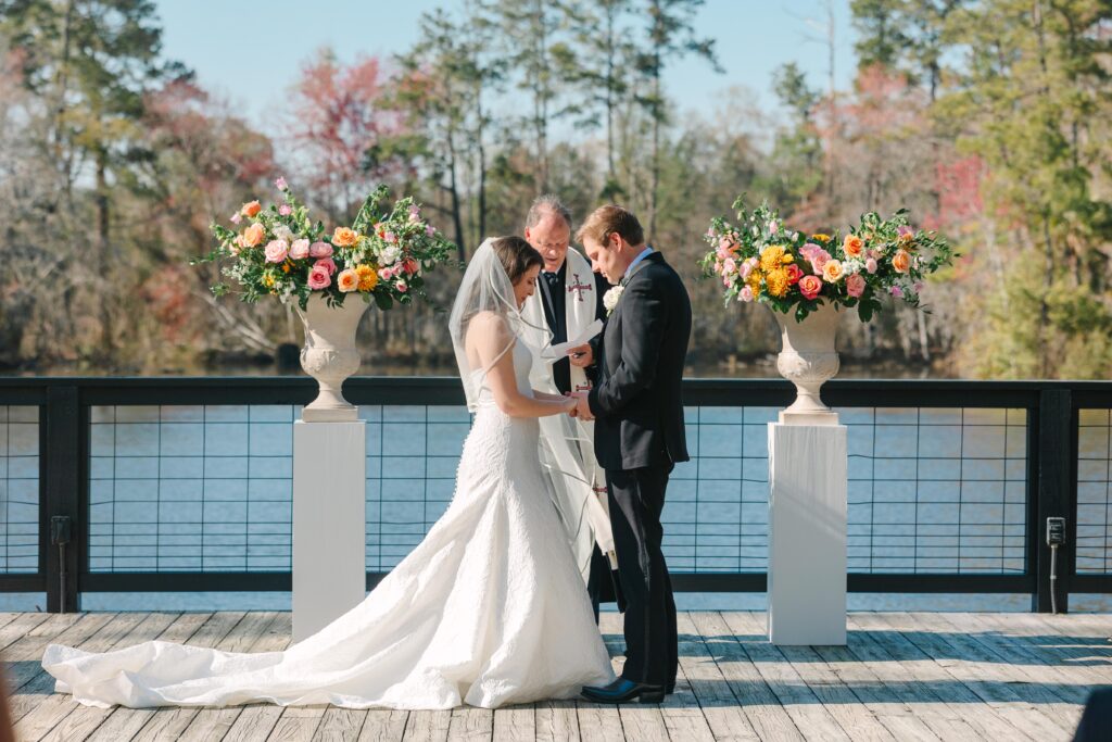 Bride and groom exchanging vows beside the water with colorful florals framing the ceremony and views reminiscent of elegant wedding venues on the water in Charleston SC.