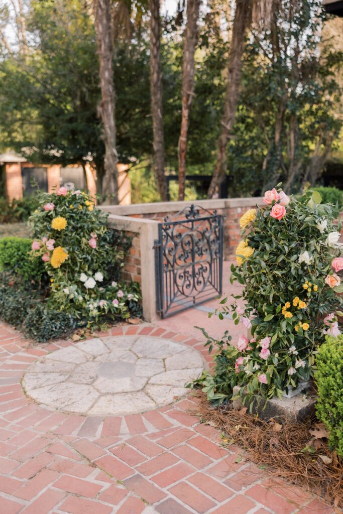 A garden ceremony space features a wrought iron gate framed by lush florals and brick pathways, setting an inviting tone often found at wedding venues near Columbia SC.