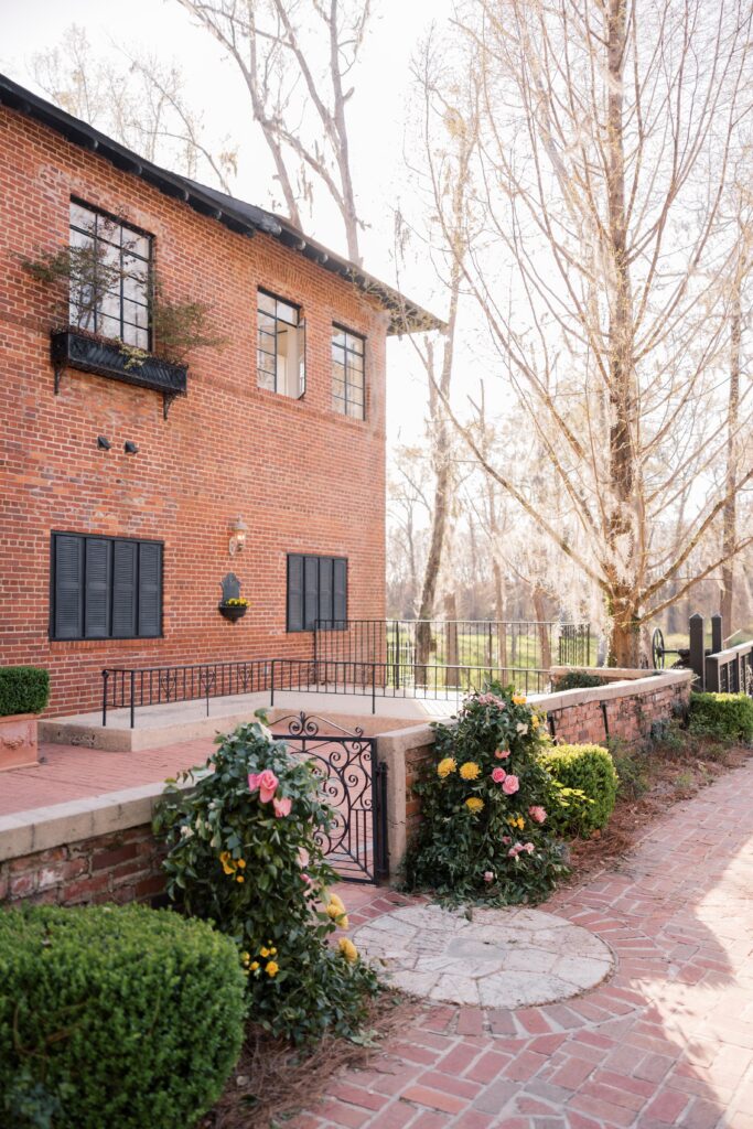 A brick building with landscaped greenery and a decorative iron gate creates a charming outdoor setting, reflecting the character of historic wedding venues in Columbia SC.