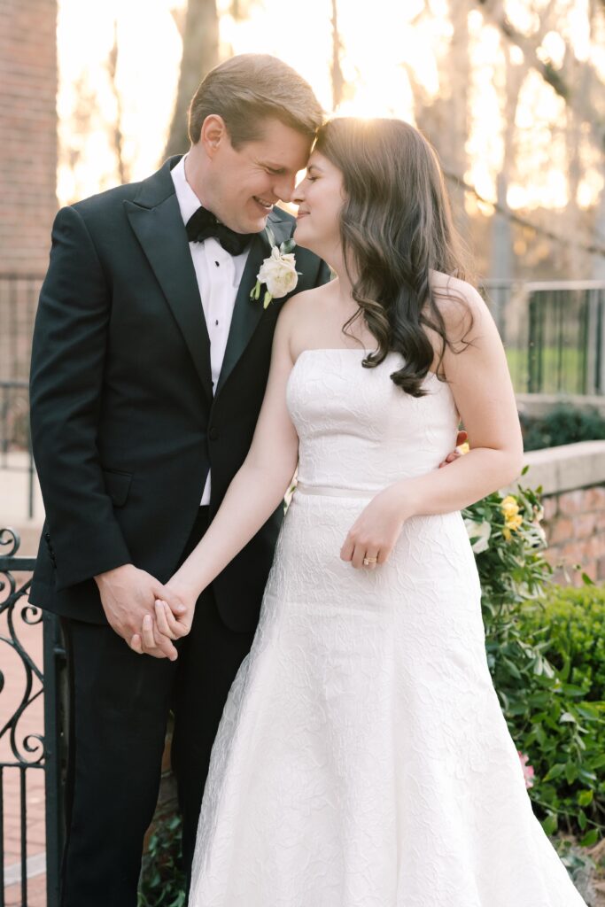 The bride and groom stand close together outdoors, smiling and holding hands as golden light frames the moment, showcasing the romantic portrait style of Columbia SC photographers.