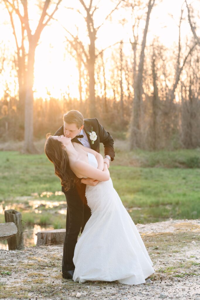 Outdoor Wedding Venues Columbia SC | Stee Garman Photography Fine-art Wedding Photographer | A couple in wedding attire shares a romantic kiss at sunset in a wooded area. The warm glow and serene setting evoke a feeling of love and joy.