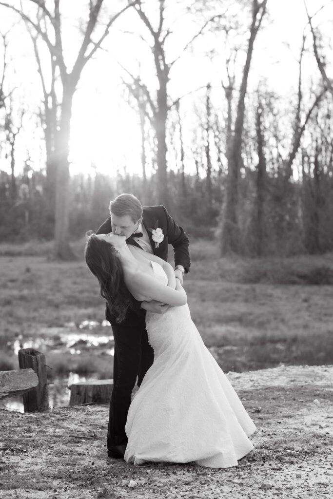 Wedding Photographer Columbia SC | Stee Garman Photography Fine-art Wedding Photographer | A couple shares a romantic dip and kiss outdoors, surrounded by a forest. The sun sets behind them.