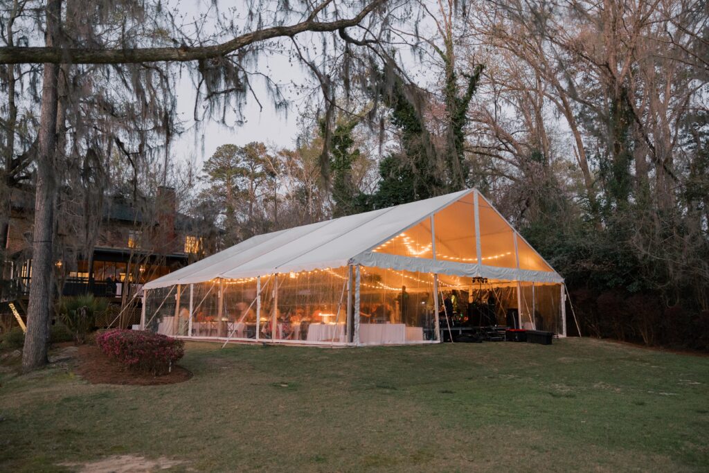 A sailcloth tent glows warmly at dusk with string lights illuminating the reception inside, reflecting the ambiance of outdoor wedding venues near Columbia SC.