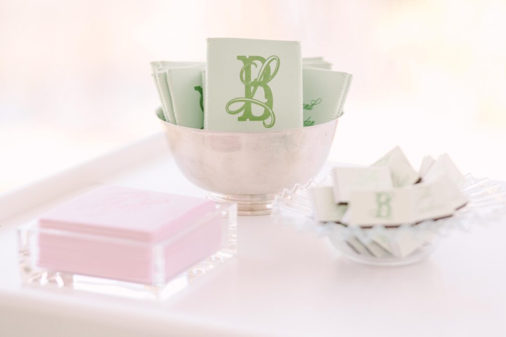 Wedding Planning in Columbia SC | Stee Garman Photography Fine-art Wedding Photographer | A silver bowl holds light green napkins with a decorative "B" in green. Nearby, a pink box sits on a soft white surface, creating an elegant, sophisticated look.
