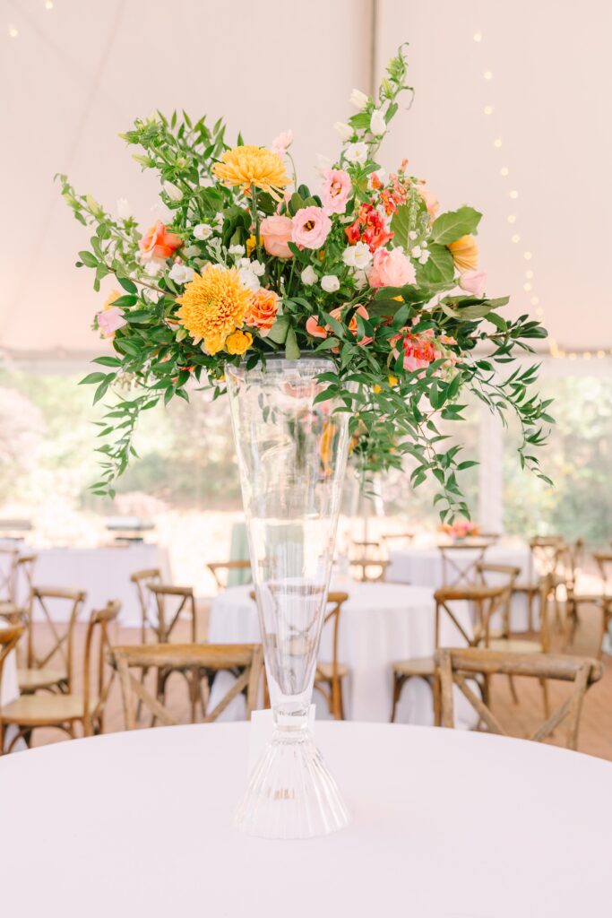 Wedding Photographer Columbia SC | Stee Garman Photography Fine-art Wedding Photographer | Elegant floral arrangement in a tall glass vase on a round table with white cloth. Vibrant pink, orange, and yellow flowers evoke a festive, summery tone.