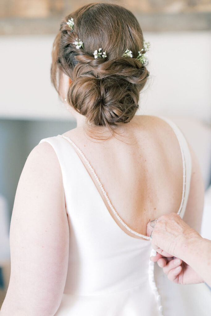 A hand fastens the bride’s gown as her floral hairpiece and low updo come into view, a quiet getting-ready moment at Wavering Place Plantation.