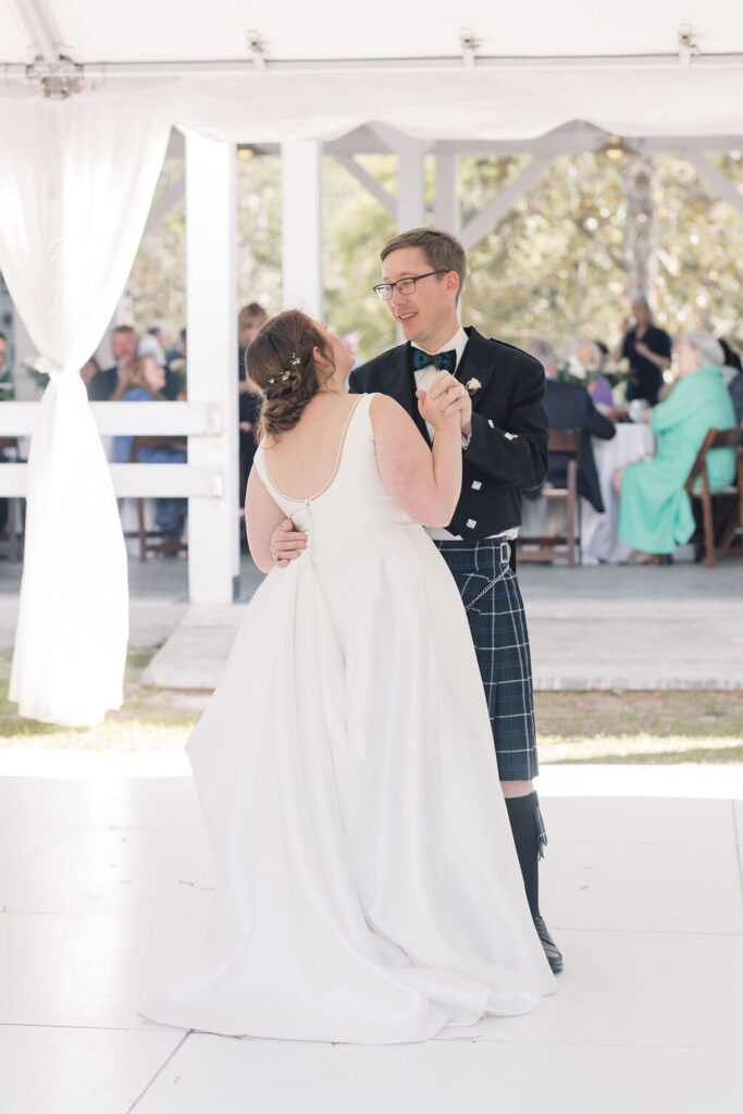 Columbia SC Wedding Photographers | Stee Garman Photography Fine-art Wedding Photographer | Bride and groom share a first dance under a white tent. The bride wears a flowing white gown, while the groom dons a kilt and black jacket. Festive, joyful atmosphere.