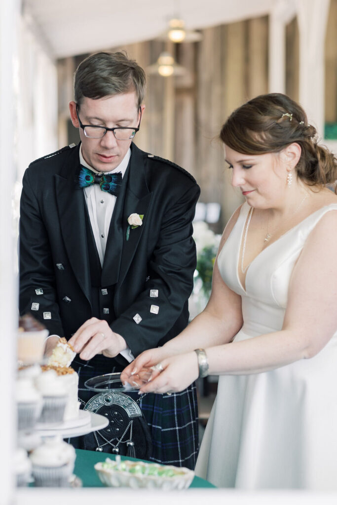 Wedding Venues in Columbia SC | Stee Garman Photography Fine-art Wedding Photographer | A couple in wedding attire smiles while cutting a cake together. He wears a kilt and jacket, she wears a white dress. The setting is bright and festive.