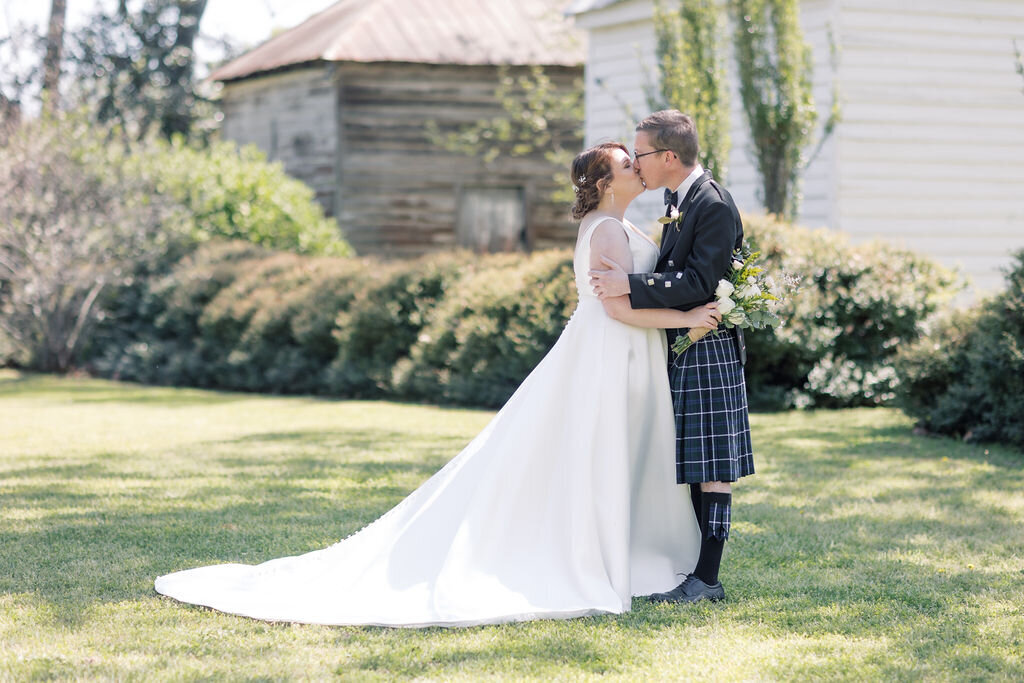 The couple shares a kiss outdoors with a rustic backdrop, capturing a soft and natural moment that reflects the style of photographers in Columbia SC.