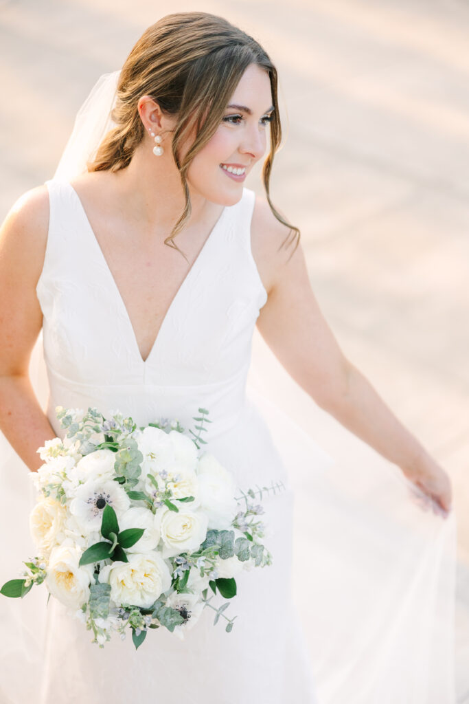 Wedding Venues in Columbia SC | Stee Garman Photography Fine-art Wedding Photographer | Bride in a white dress holding a bouquet of white roses and greenery, smiling gently. Soft lighting creates a romantic, elegant atmosphere.