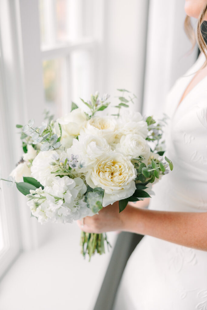 Wedding Planning in Columbia SC | Stee Garman Photography Fine-art Wedding Photographer | A bride holds a bouquet of white and cream roses mixed with eucalyptus and greenery. The scene conveys a soft, romantic, and elegant tone.