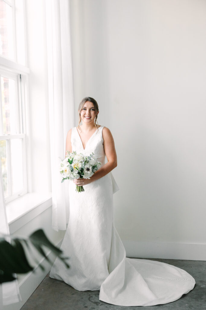 Soft natural light fills a minimalist room as a bride holds her bouquet near a window, showcasing the quiet beauty found in intimate wedding venues in Columbia SC.