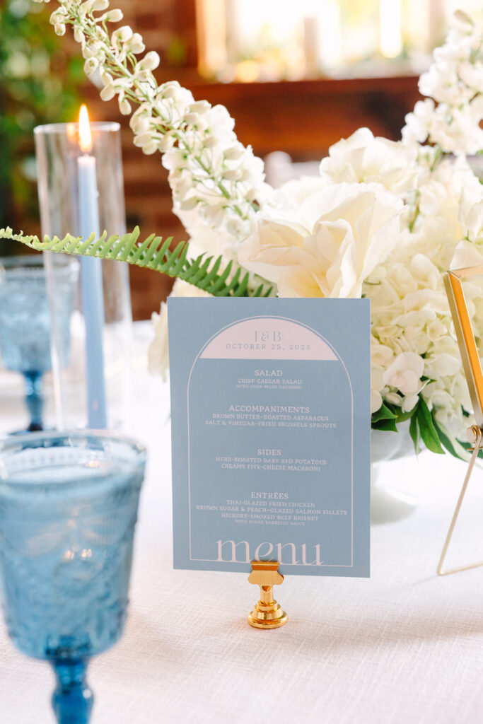 Wedding Reception Venues in Columbia SC | Stee Garman Photography Fine-art Wedding Photographer | Elegant table setting with blue menu, surrounded by white flowers and greenery. A lit blue candle and blue goblet create a serene ambiance.