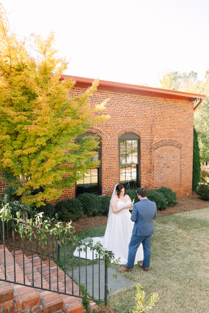 Wedding Venues Columbia SC | Stee Garman Photography Fine-art Wedding Photographer | Bride and groom exchange vows outside a brick building with arched windows. A tree with yellow leaves adds warmth to the romantic scene.