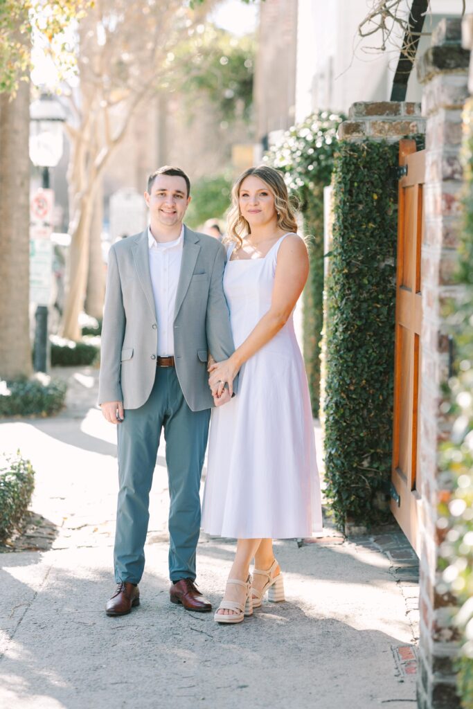 Engagement Photo Locations Columbia SC | Stee Garman Photography Fine-art Wedding Photographer | A couple stands on a by green wall. The woman in a white dress gazes at the man in a light grey blazer, both appearing happy and relaxed.