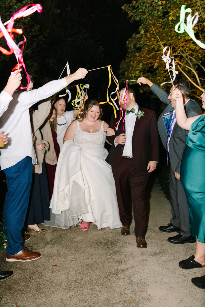 Hampton Preston Mansion Wedding | Stee Garman Photography Fine-art Wedding Photographer | Bride and groom joyfully walk through a group of guests at night. Guests wave colorful ribbons, creating a festive and celebratory atmosphere.