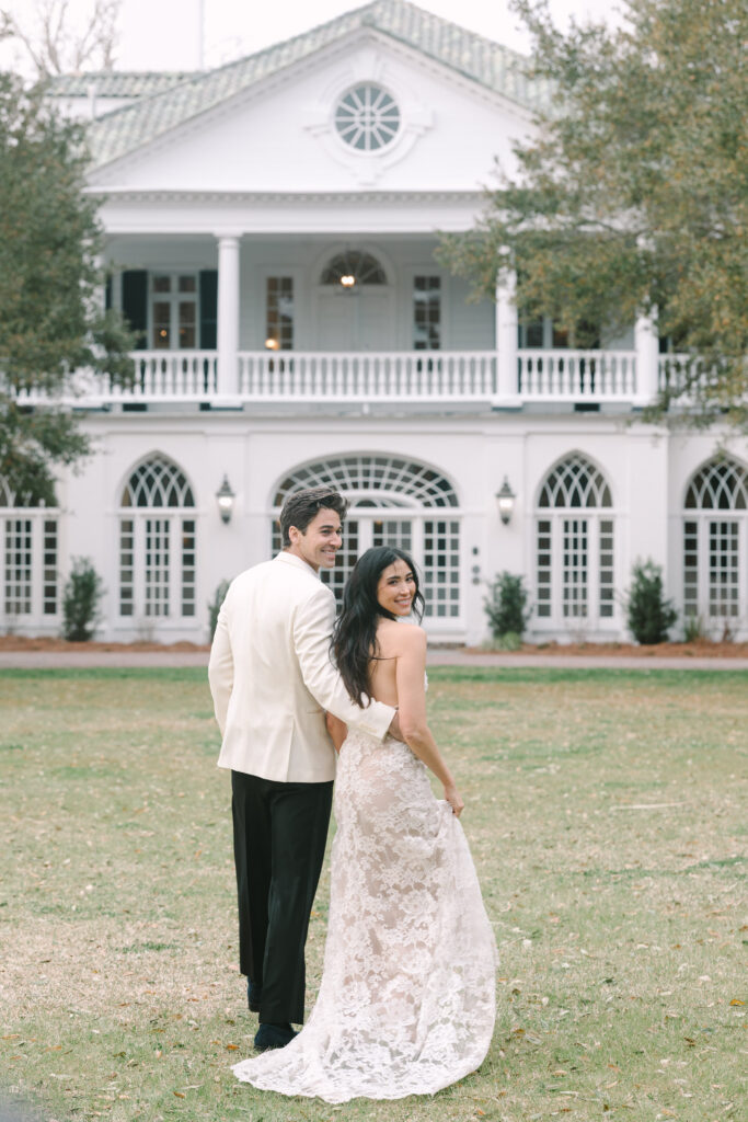 Couple posing in front of a grand white estate with classic Southern architecture and manicured grounds at one of the most iconic Charleston wedding venues on the water.